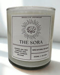 Candle labeled 'The Sora' with a label on a white surface